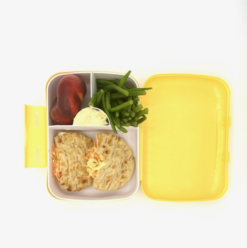 NjaNja gezonde lunchbox op school geleverd: volkoren veggie pitabroodje, perzik, boontjes, hummus