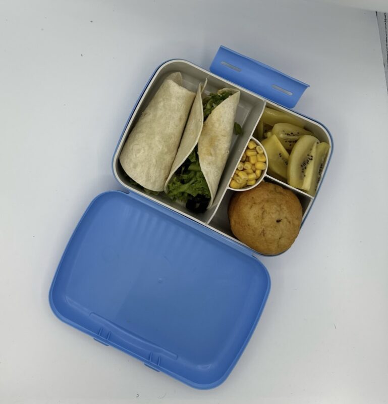 NjaNja gezonde lunchbox op school geleverd: volkoren veggie wrap, kiwi, pompoen muffin, maïs
