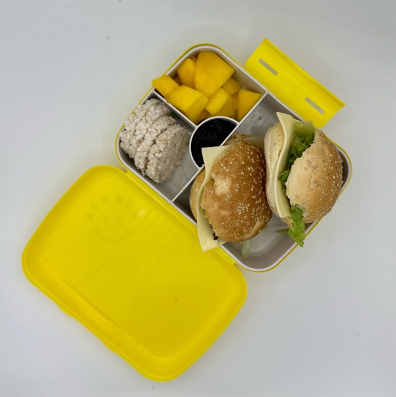 NjaNja gezonde lunchbox op school geleverd: volkoren sandwich kaas en groenten, mango, rijstcrackers, rozijnen